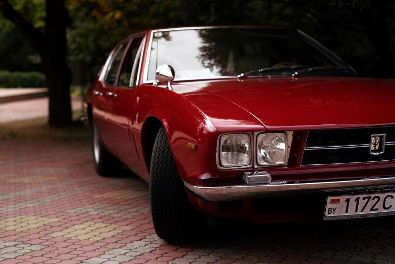 a red and shiny old style car is parked on a cobblestone road