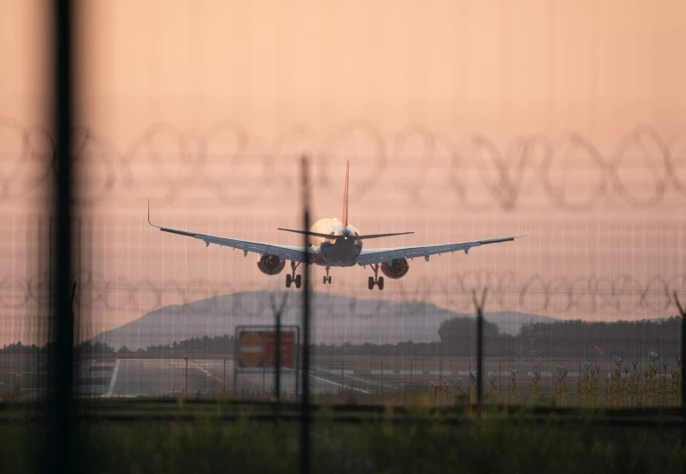 a plane flies low by a fence in front of mountains