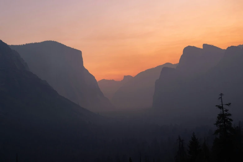 the sun sets over a mountain and a valley with trees