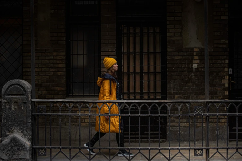 a man wearing a yellow coat and standing in front of a fence