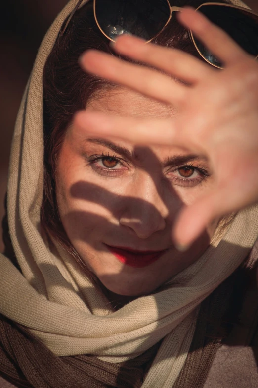 a woman wearing a scarf and sunglasses and holding her hand in front of her face