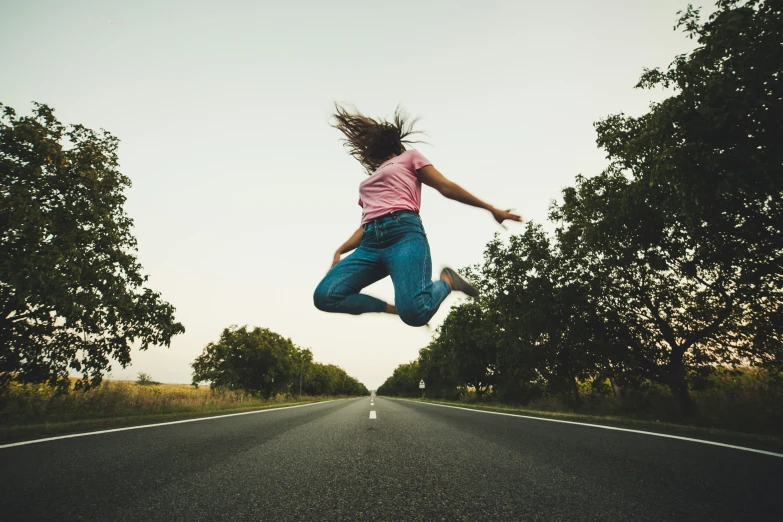 a girl leaps into the air while riding down an empty road