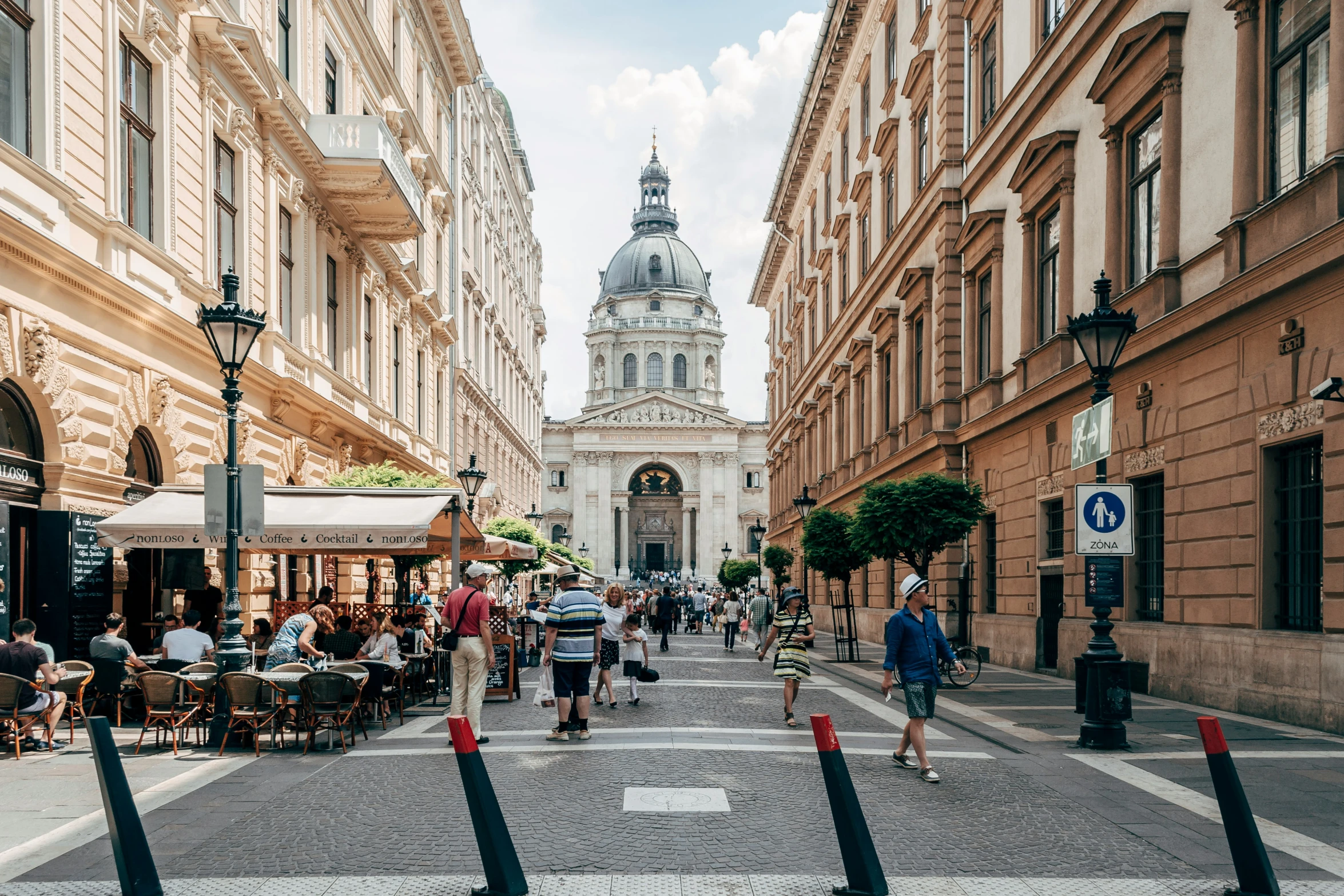 people walk down a city street lined with tall buildings