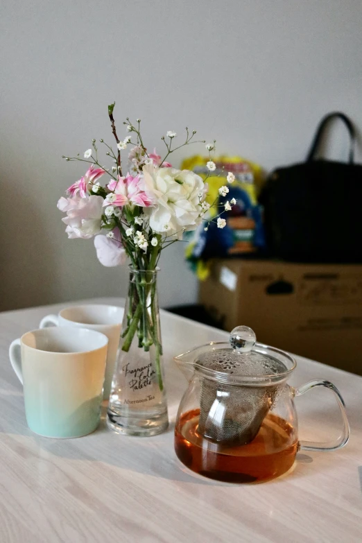 a clear tea pot, small pitcher of flowers and a cup of tea on a table