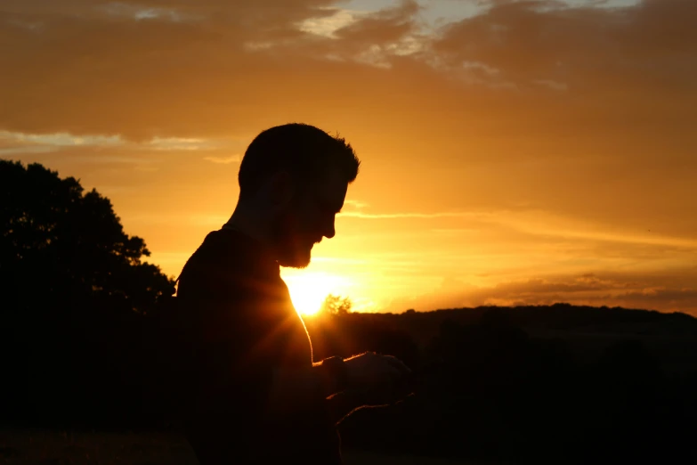 the silhouette of a man holds his cell phone as the sun goes down