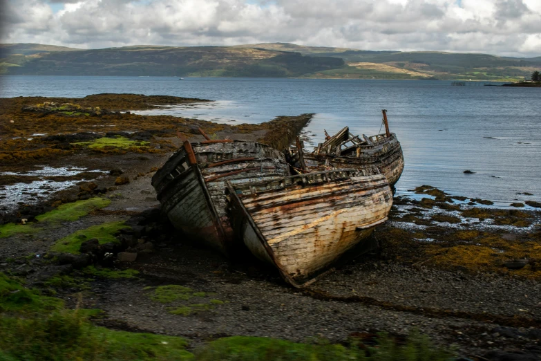 an old rusty boat sits at the edge of some grass