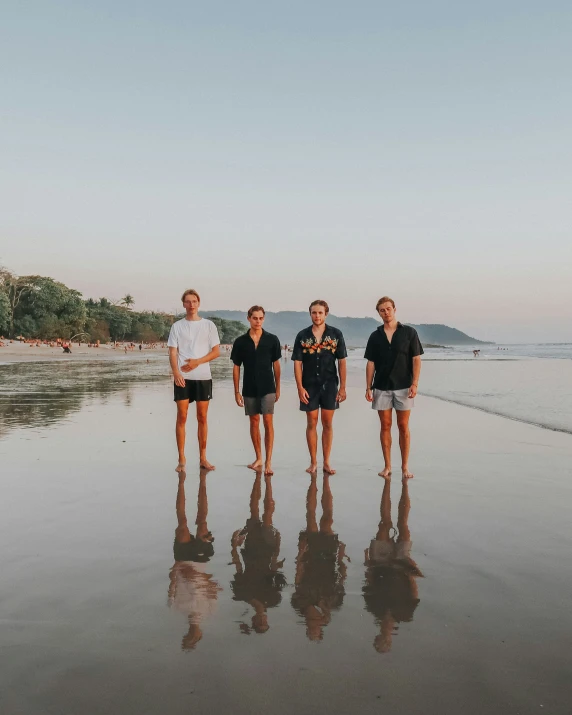 five young men standing on the beach near the ocean