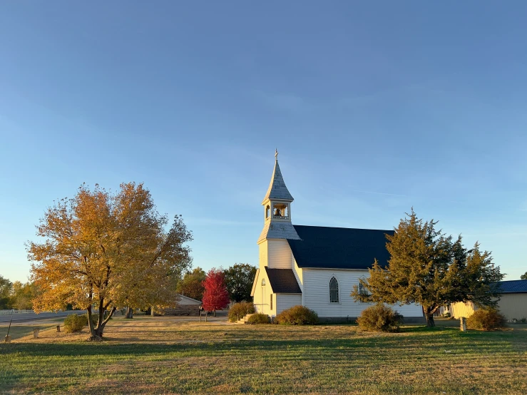 a white church with a black roof surrounded by autumn trees