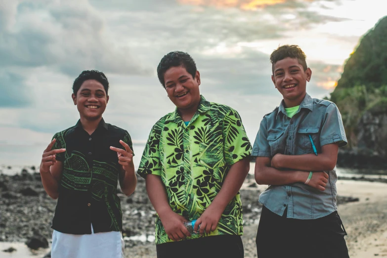 three boys standing beside the ocean in colorful shirts