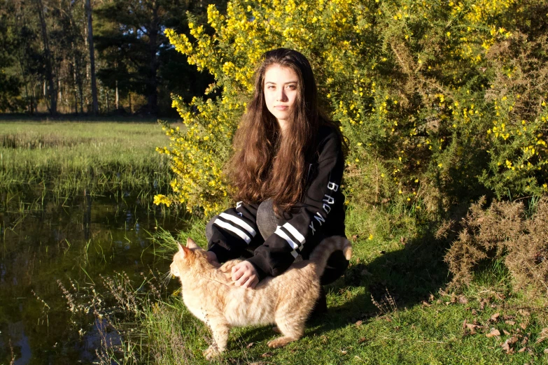 a beautiful woman sitting in front of a lake while holding a cat