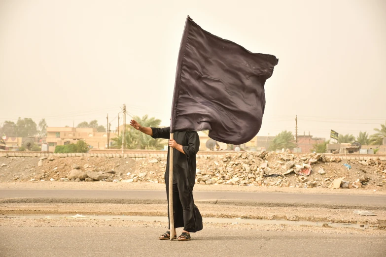 the man carries a big black cloth across the street