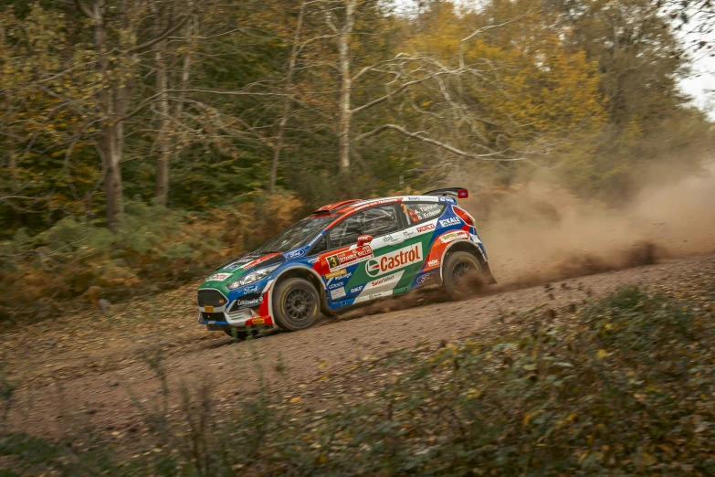 the colorful rally car is making its way down a muddy dirt road