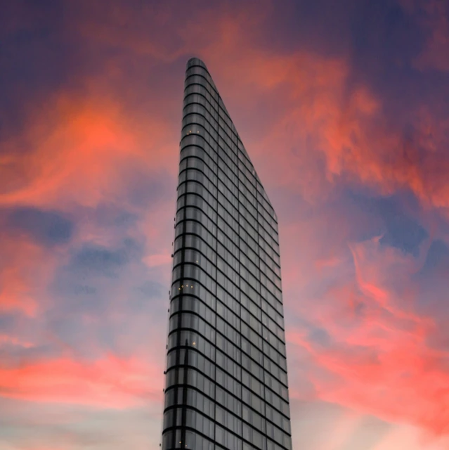 a tall glass building on top of a hill under a cloudy sky