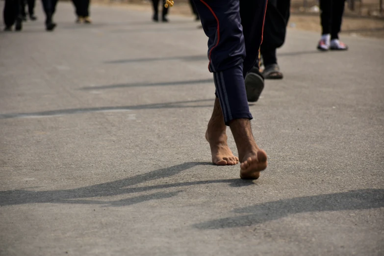 barefoot people walking across a parking lot with a child sitting on a bench