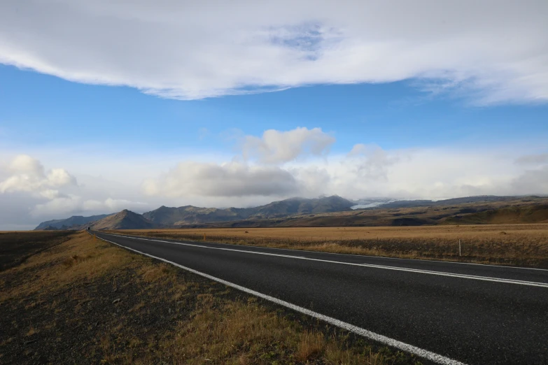 a road runs parallel to the horizon and through grassy fields