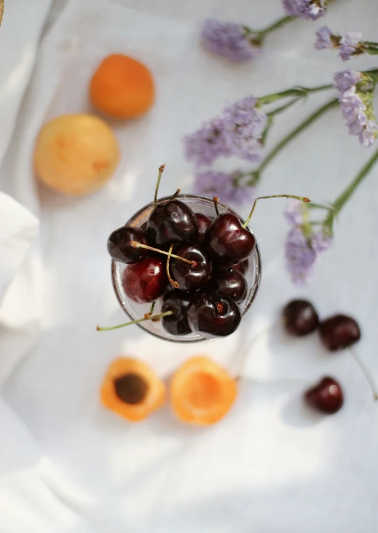 some cherries in a bowl and some tangerines on a table