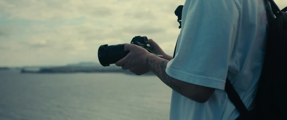 a person holding a camera next to the ocean