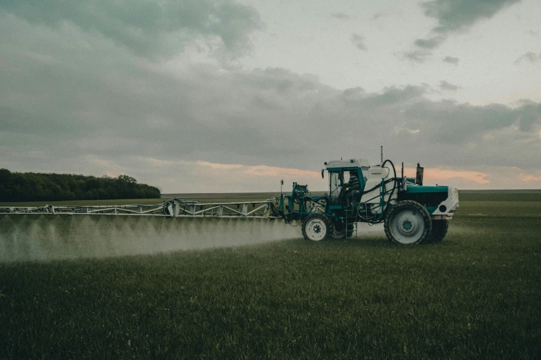 tractor sprays crops in a large field on a cloudy day