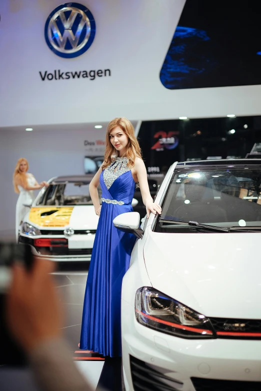 a woman is posing in front of a volkswagen car