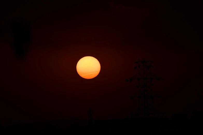 the sun shines as it rises behind several power lines