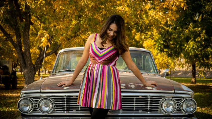 an attractive young woman standing next to an old car