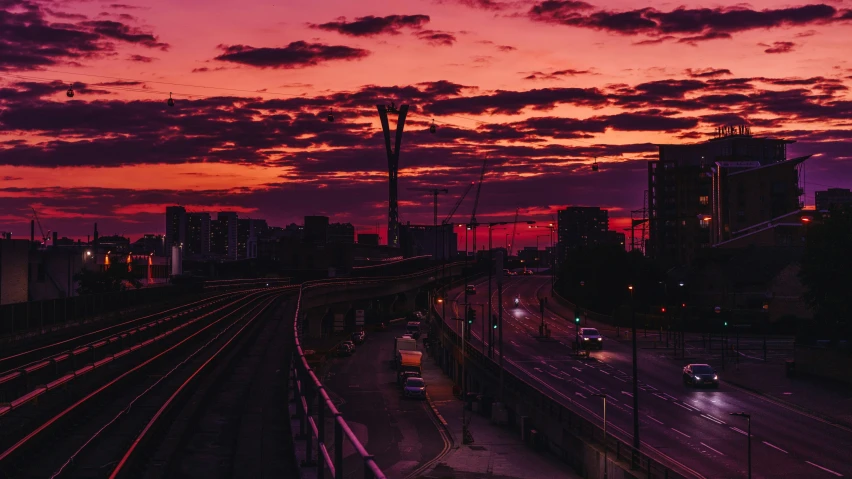 a sunset view of a city street with cars on the road and a train track with lights going down