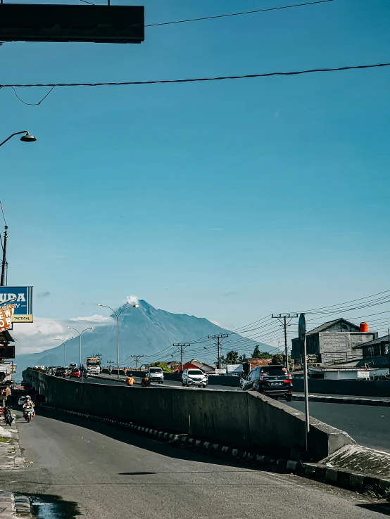 people walking on an urban street in front of a tall mountain