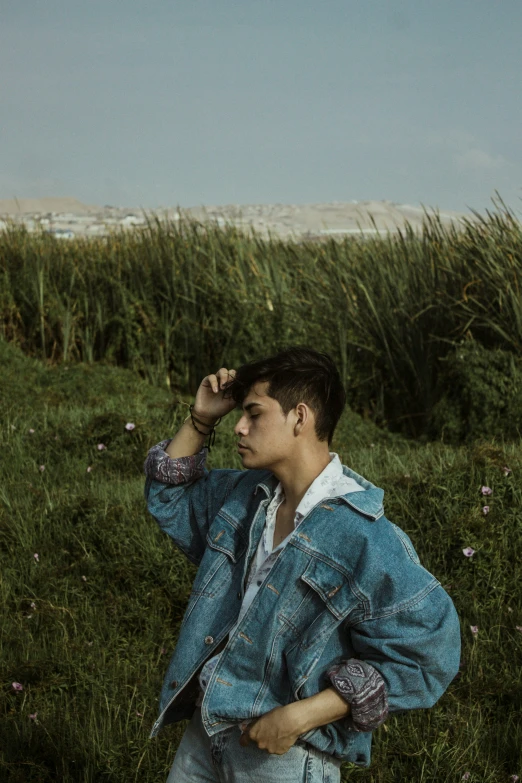 a man in jeans stands in a green grass field, while talking on a cell phone