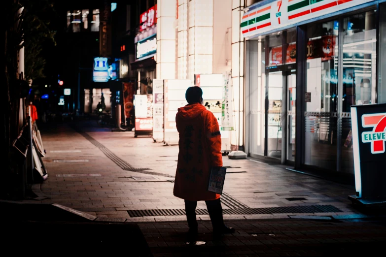 a person stands in a city street in front of store fronts at night