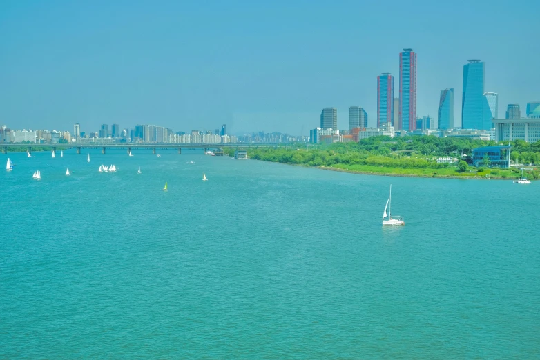 sailboats in the middle of a river with tall buildings on either side