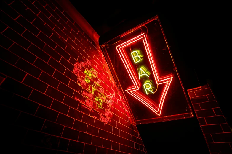 a red neon bar sign lit up against a brick wall