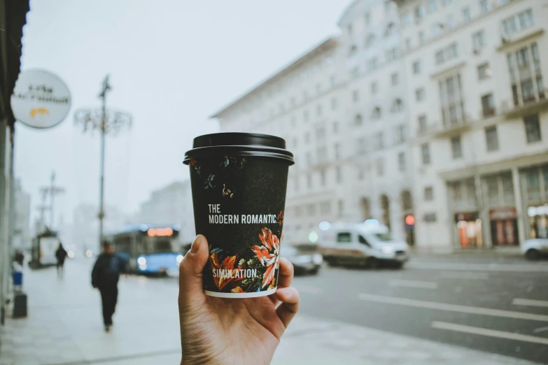 person holding up a cup of coffee on the sidewalk