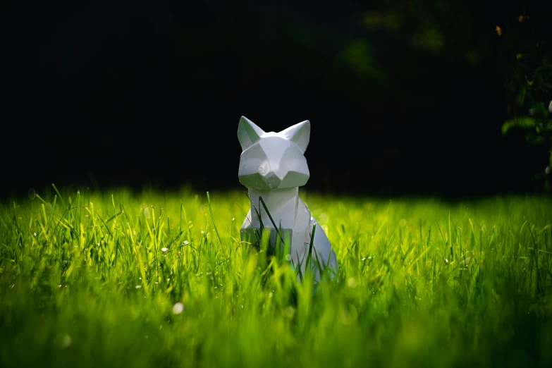 a white cat made out of paper on top of a lush green field