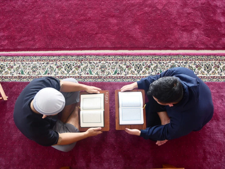 two men are reading their book on a large rug