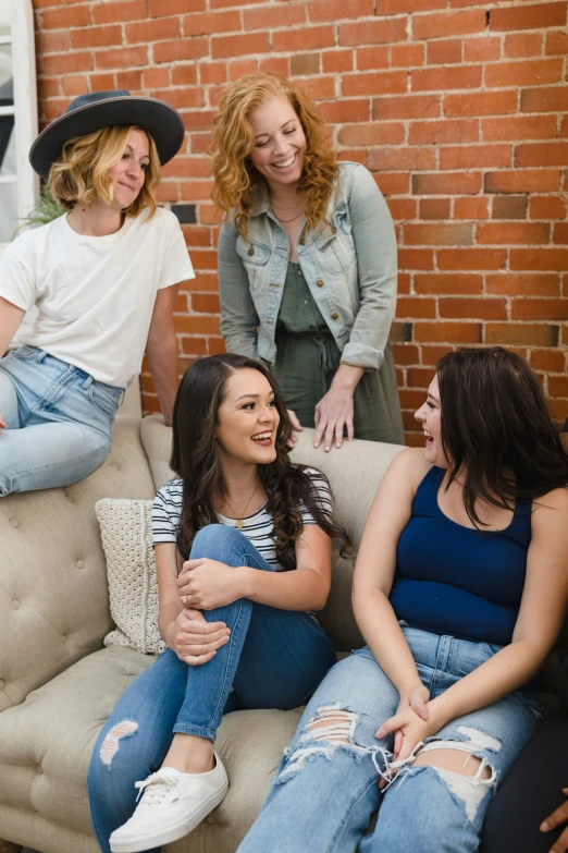 three women on a couch laugh as one of them sits next to the other