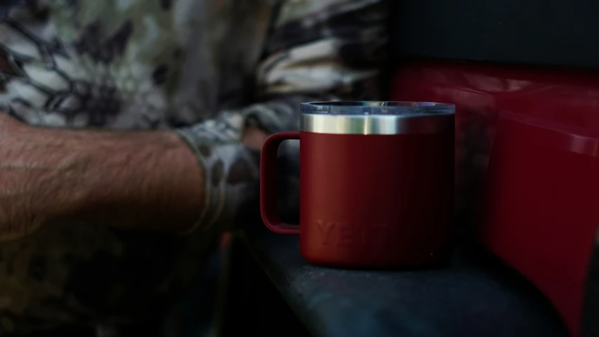 a man is sitting on a bench holding a red coffee mug