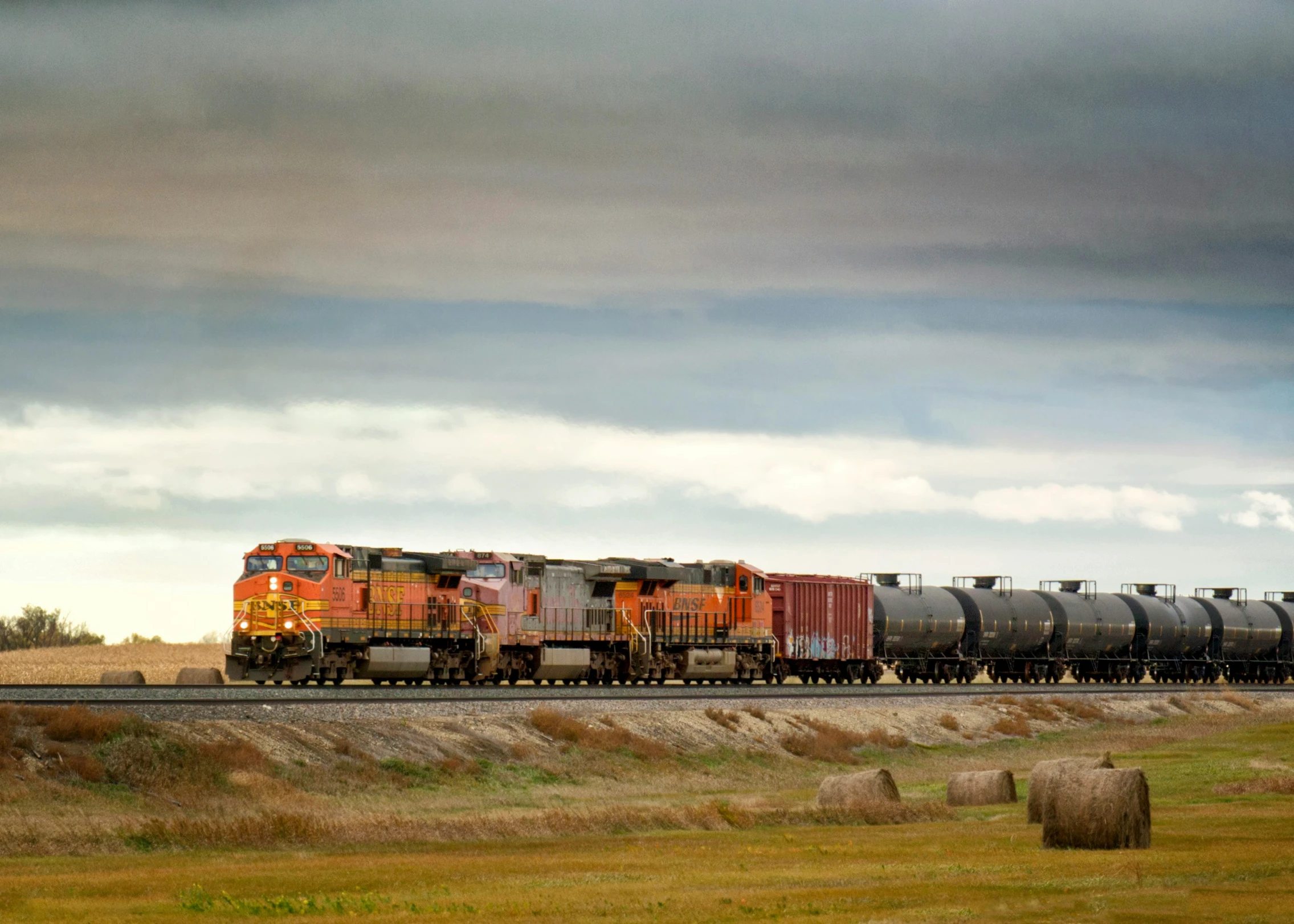 a train traveling down the track with bales of hay nearby