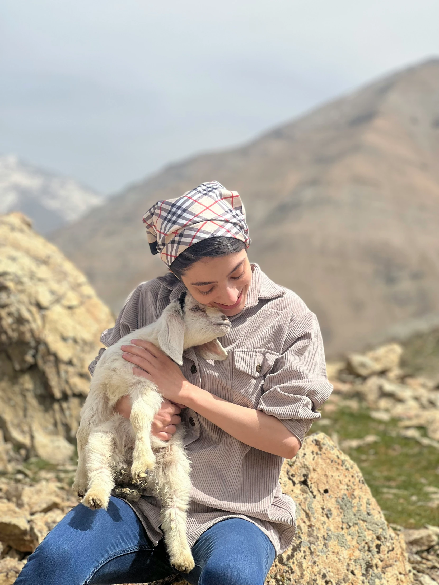 a woman holds her dog on the rocks near some mountains