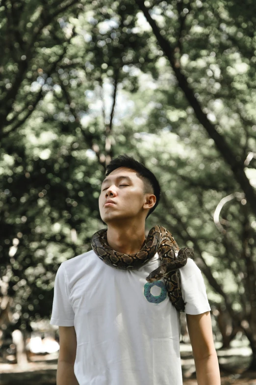 a man with a snake on his neck stands in a park