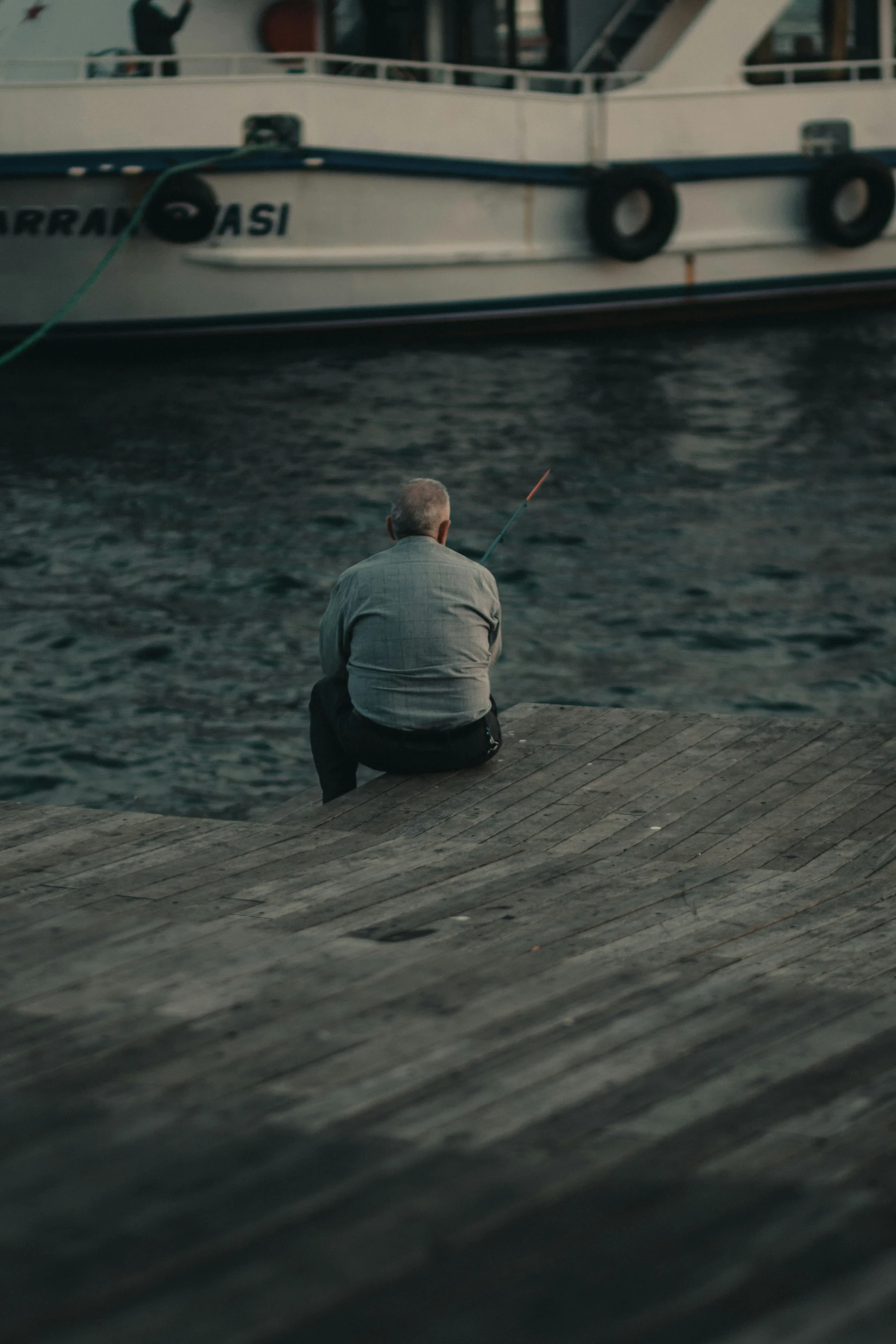 the man is kneeling down on the dock looking at the water