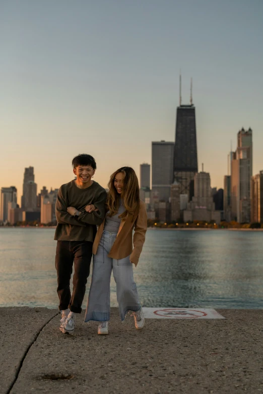 two people are standing near the water in front of city buildings