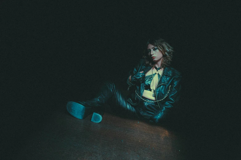 a woman in a leather jacket sits on a wood floor