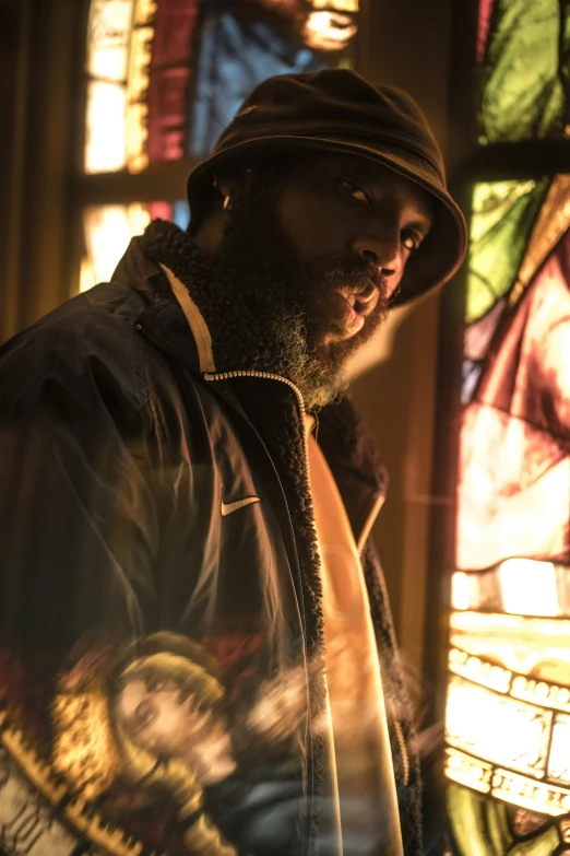 a man wearing a hat standing next to a stained glass window