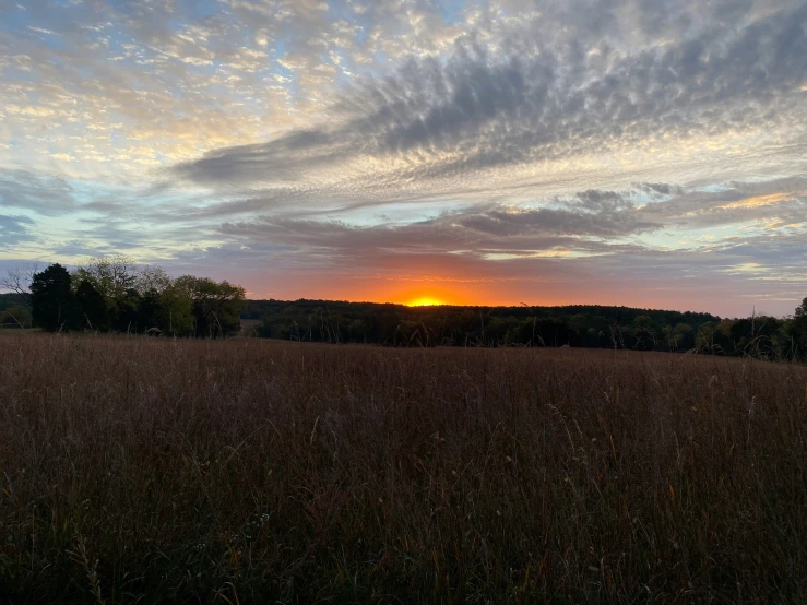 an empty grassy field at sunset with clouds