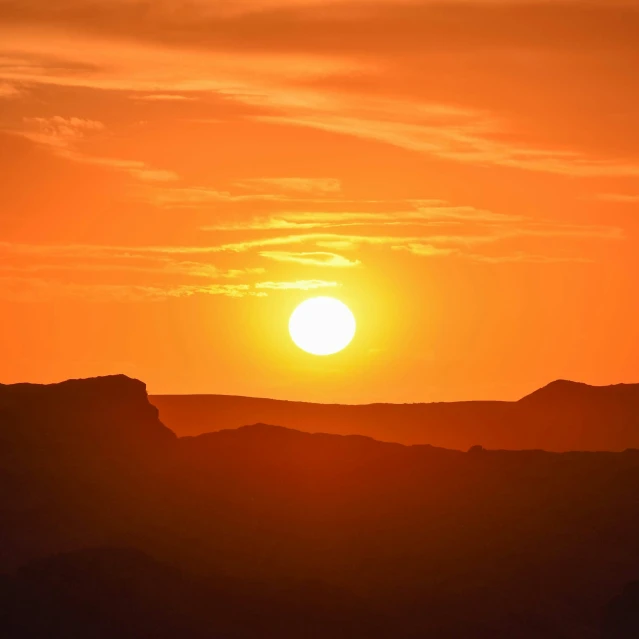 the sun rises over mountains in a bright orange sky