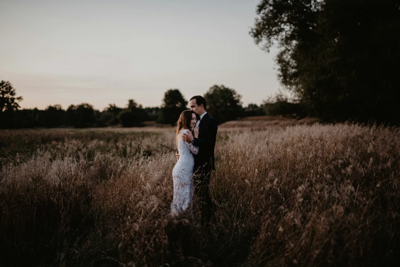 two brides emcing in the tall grass while one looks at her cell phone