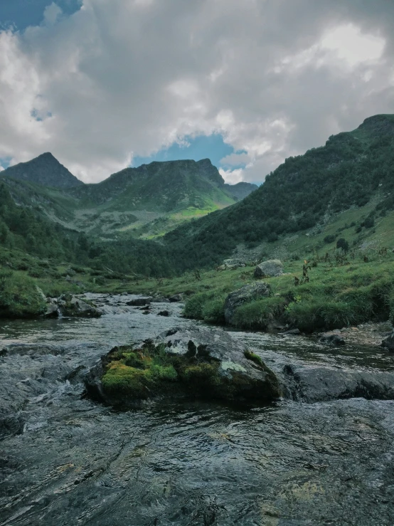 a stream runs through a grassy valley with mountains in the background