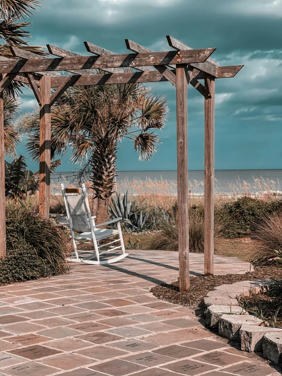 a white lawn chair under a pergolic arbor next to the ocean