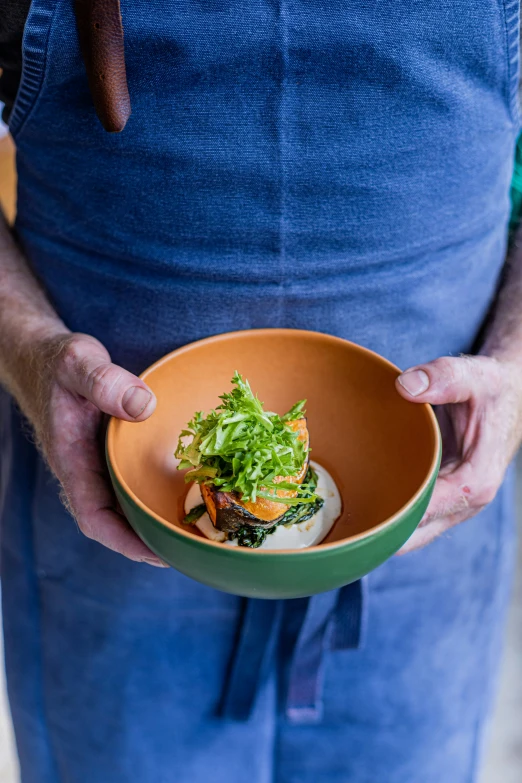 a person in aprons holding a bowl with a sandwich