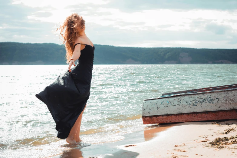 a woman standing on a beach with a boat in the ocean